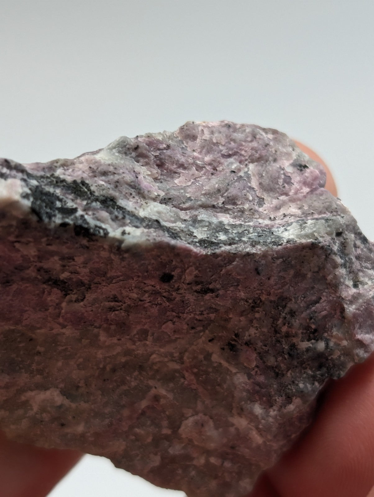A rough, irregularly shaped piece of pinkish-purple and gray mineral rock with visible striations.