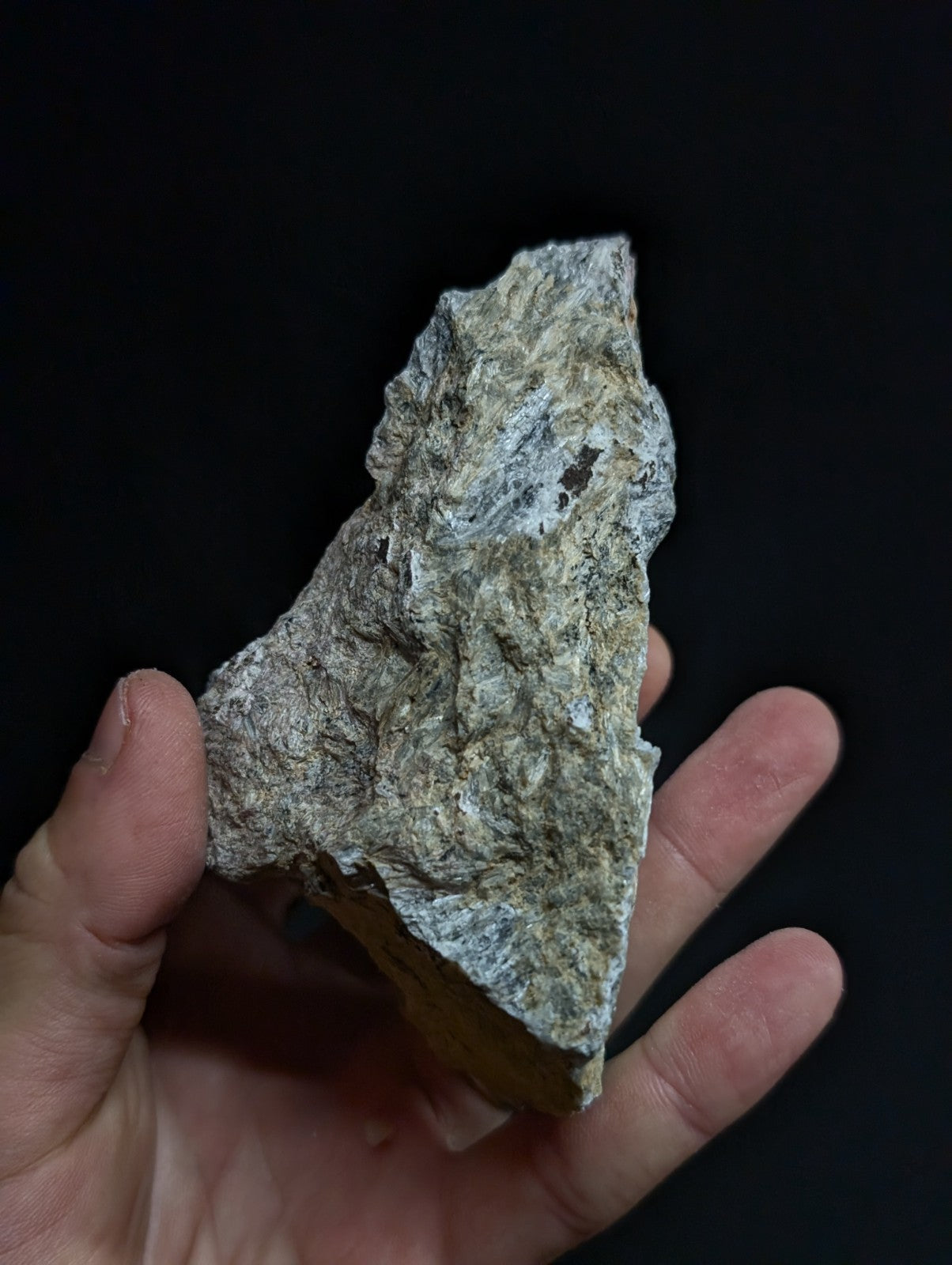 A rough, irregularly shaped grayish-green rock with a textured surface held in someone’s hand.