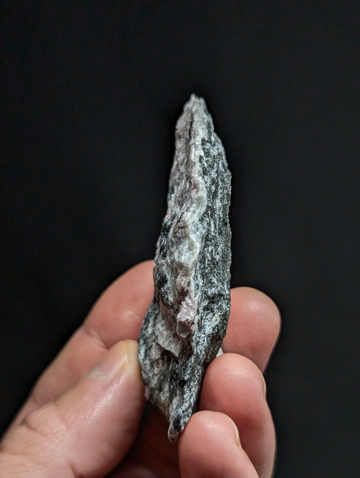 A rough, irregularly shaped gray rock with speckled white and dark mineral veins.