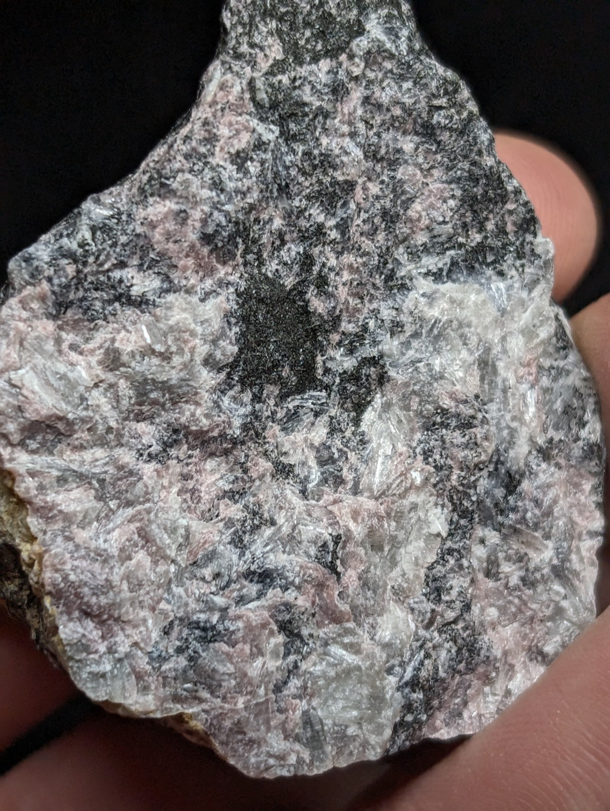 A rough, irregularly shaped rock with a mottled surface of gray, black, and pinkish hues.