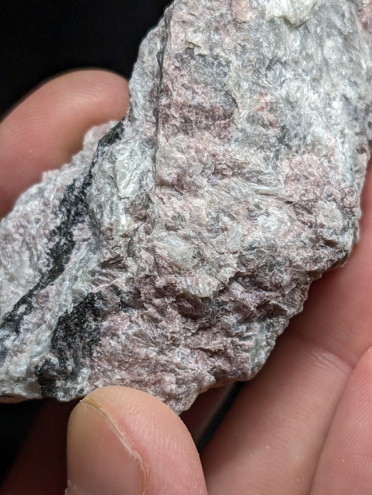 A rough, irregularly shaped rock with a mottled surface of gray, pinkish hues, and dark streaks.