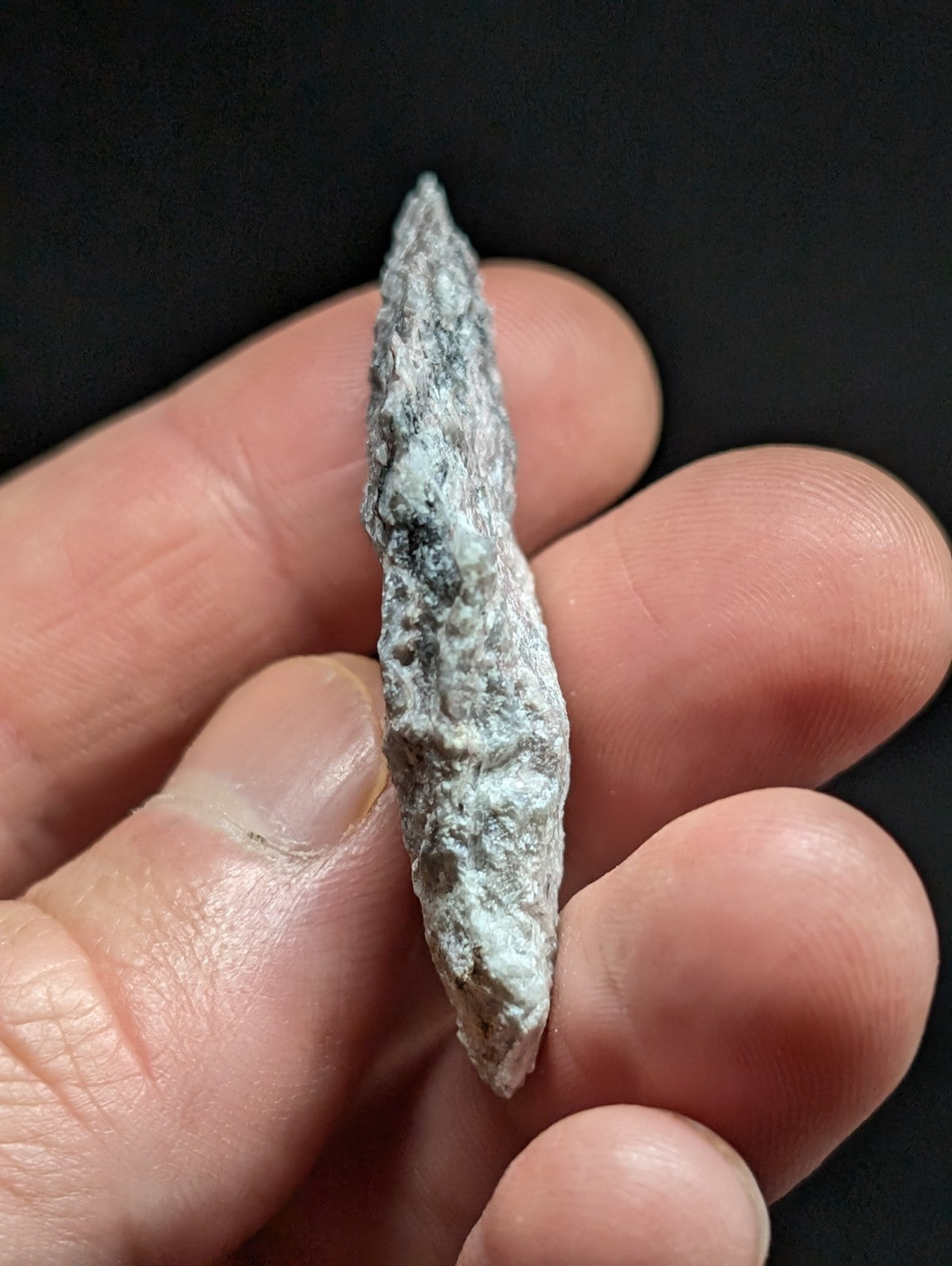 A weathered, greenish-blue patina-coated bronze arrowhead with a pointed tip and textured surface.