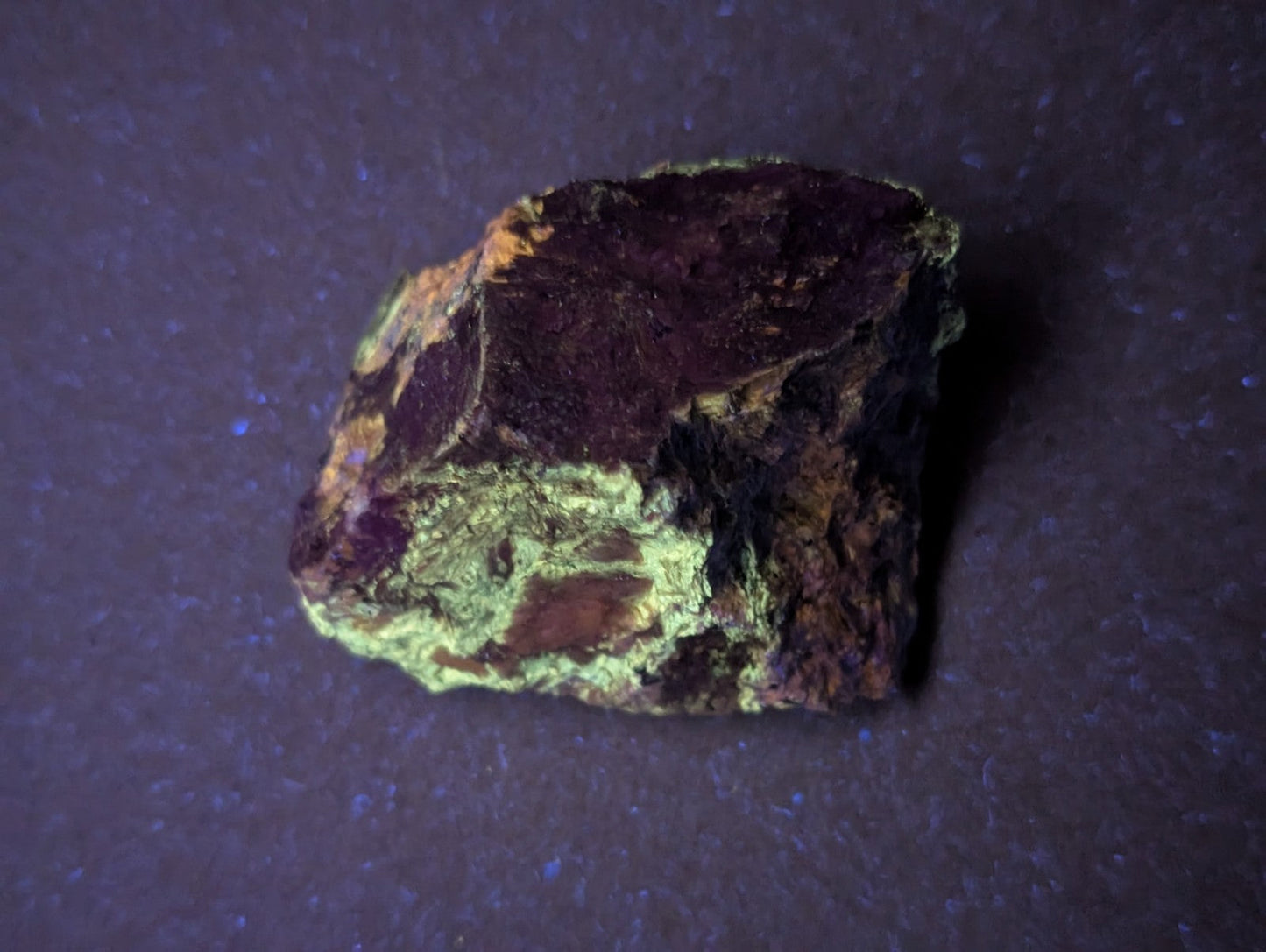 A rough, irregularly shaped mineral specimen with a deep purple to black base and patches of vibrant green veining.