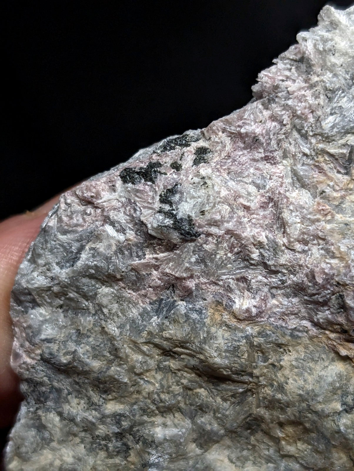 A rough, irregularly shaped rock with a mottled surface of gray, white, and subtle pinkish hues.