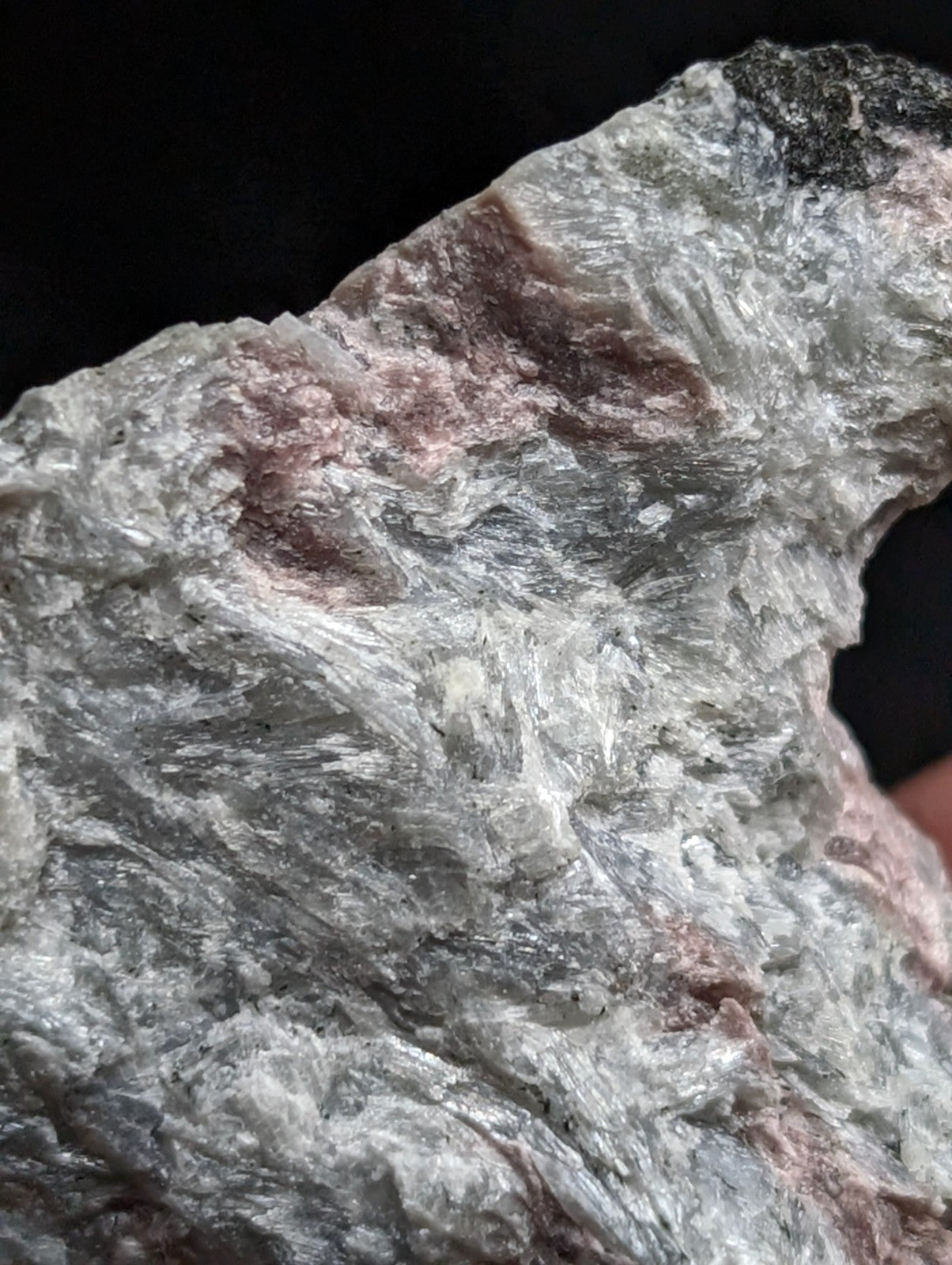 A rough, naturally occurring mineral specimen with a textured surface displaying shades of gray and subtle pinkish-brown patches.