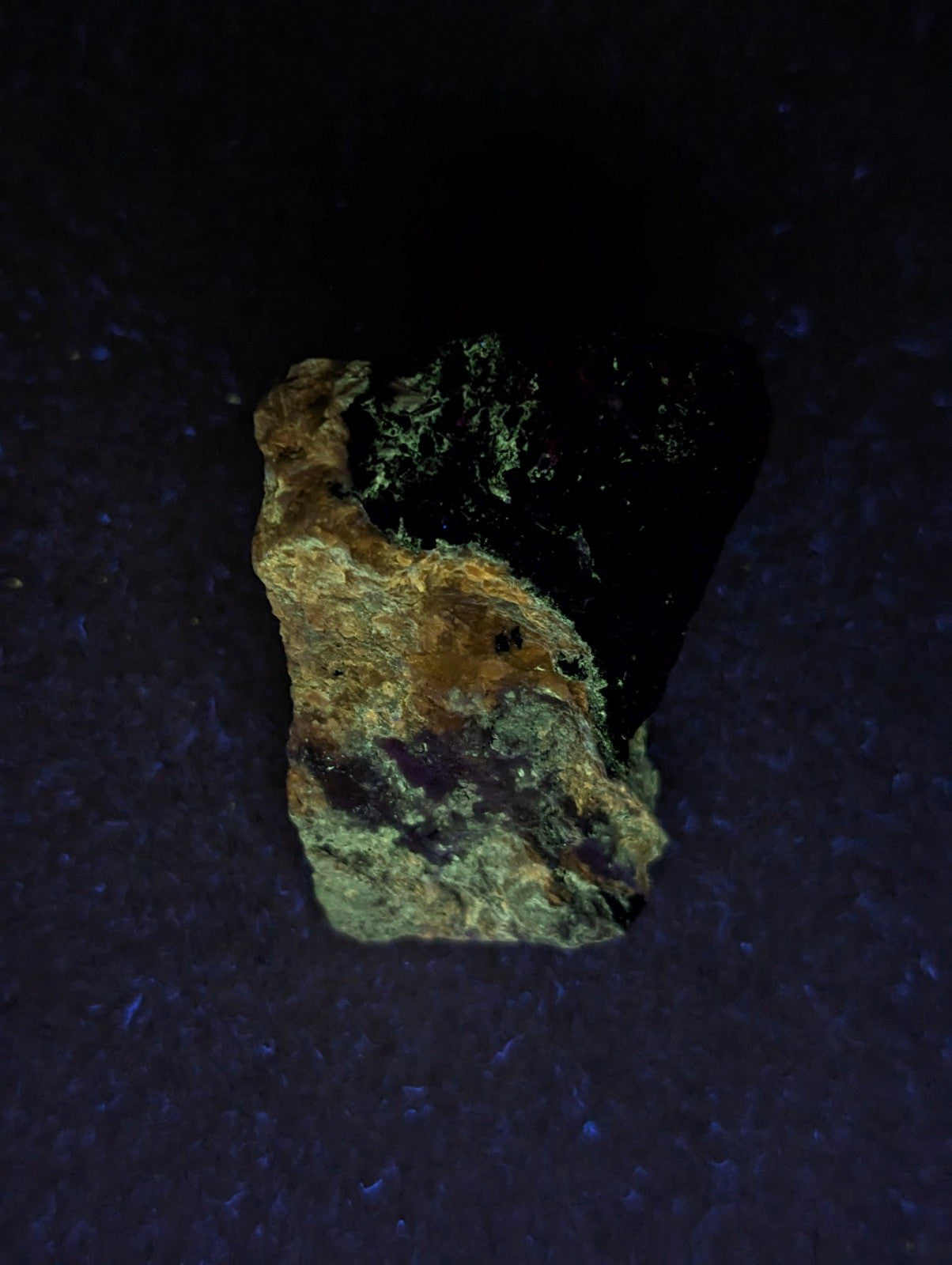 A rugged, irregularly shaped rock with a dark black core and patches of greenish-yellow mineral coating.