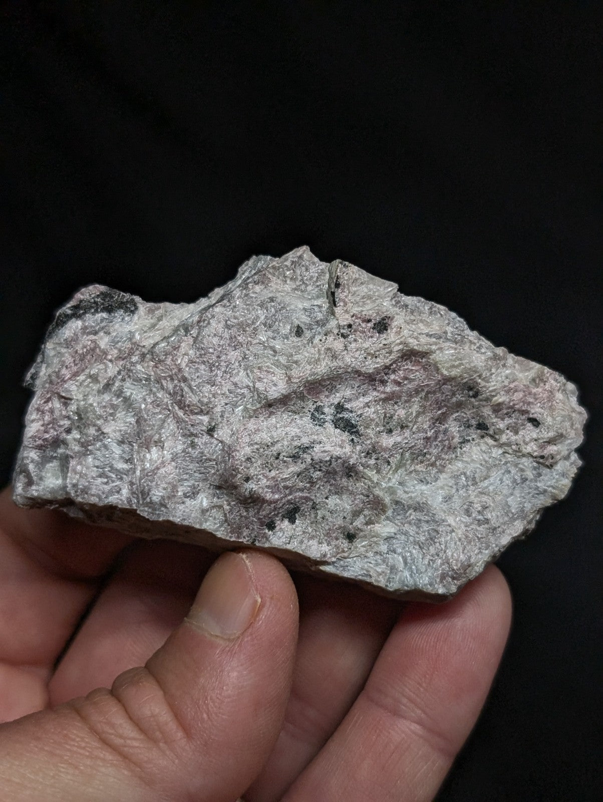 A rough, irregularly shaped gray rock with speckles of black and subtle pinkish hues.