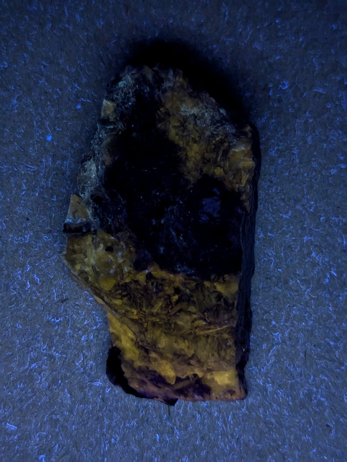 A rugged, irregularly shaped piece of mineral with a dark, almost black center and vibrant yellowish-gold streaks across its surface.