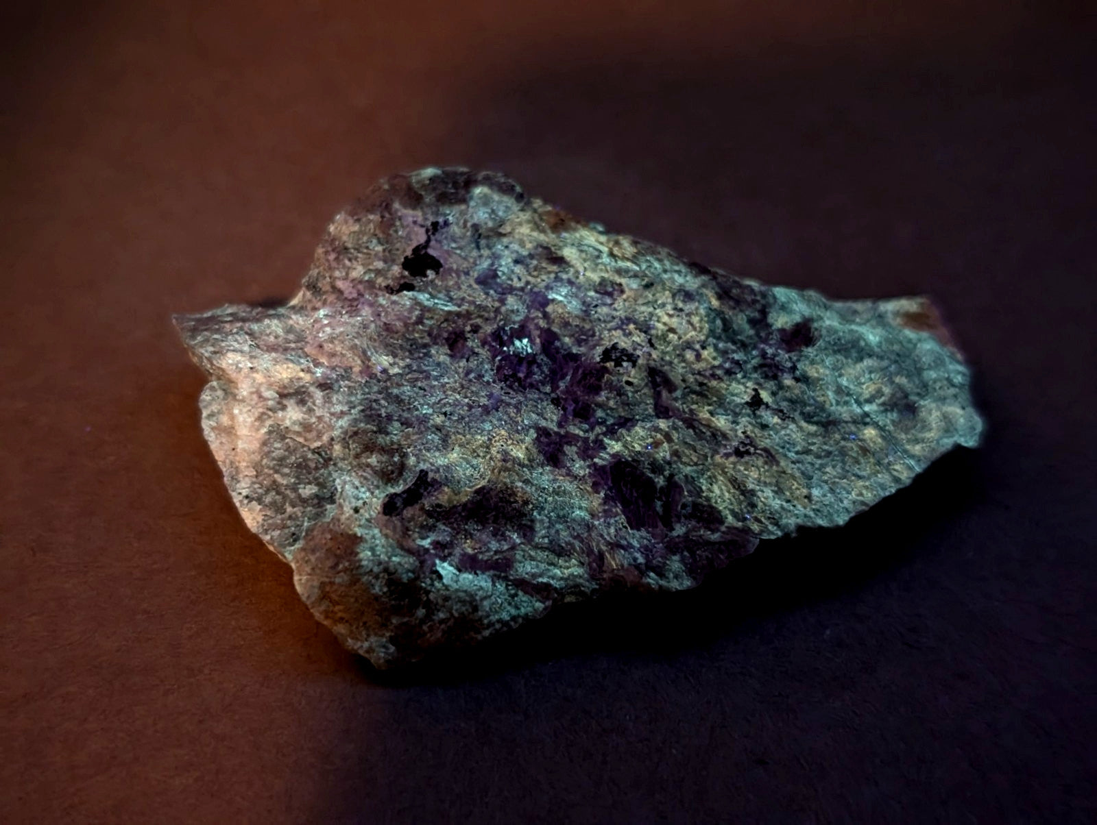 A rough, irregularly shaped rock with a mottled surface of greenish-gray and dark purple patches.