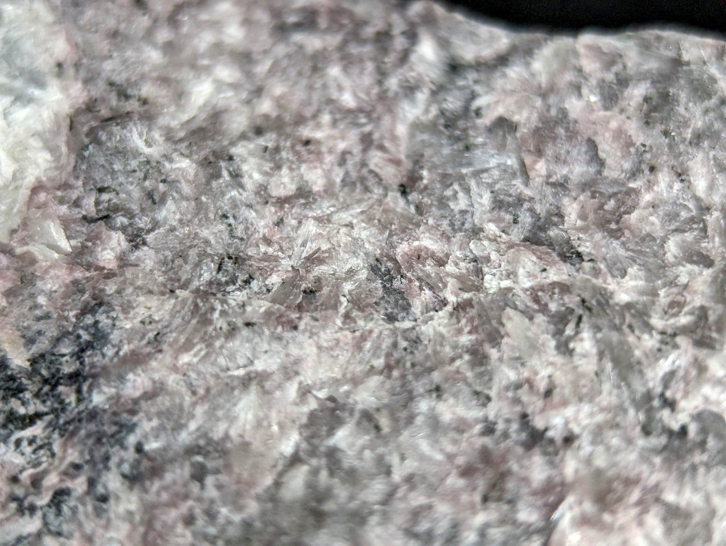 A speckled granite rock with a mottled pattern of gray, white, and subtle pinkish hues.
