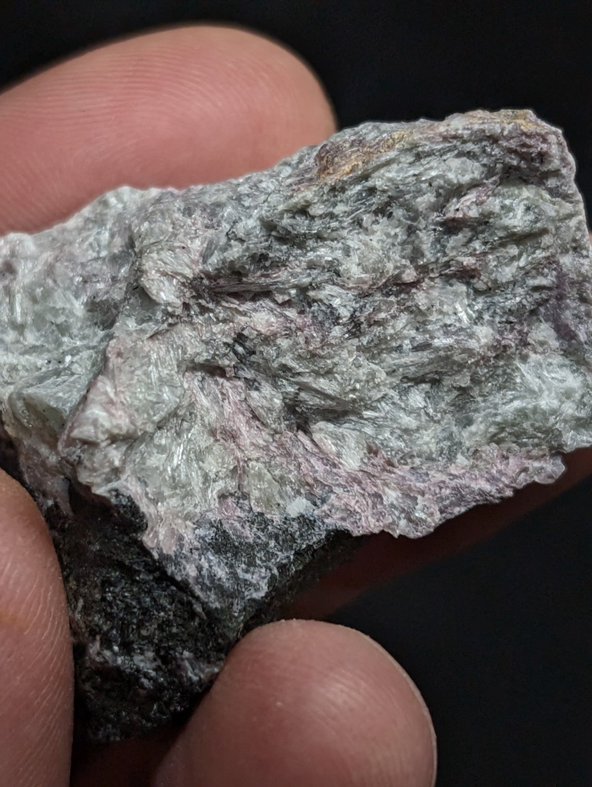A rough, irregularly shaped mineral specimen with a mottled gray and pale green surface accented by subtle pinkish hues.