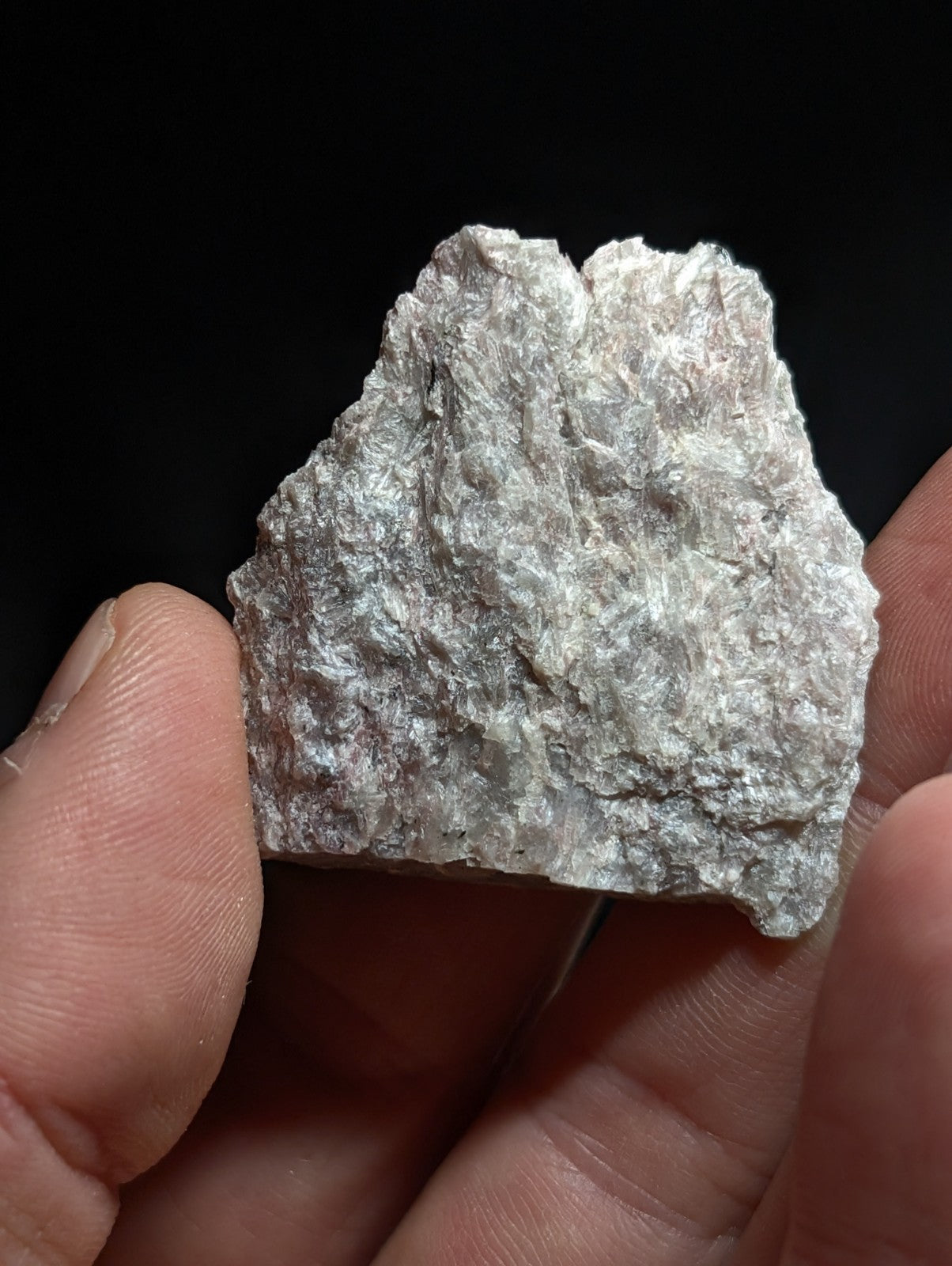 A rough, irregularly shaped piece of silver-colored mineral held in a hand.
