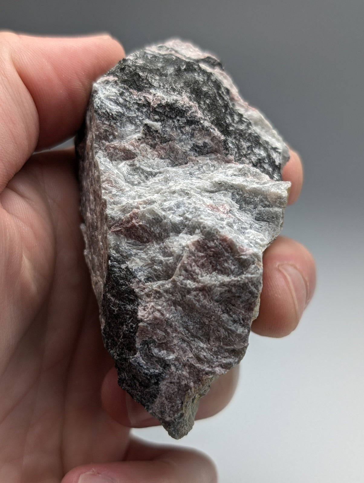 A rough, irregularly shaped miserite and wollastonite stone with mottled gray and white surface held in hand from arkansas