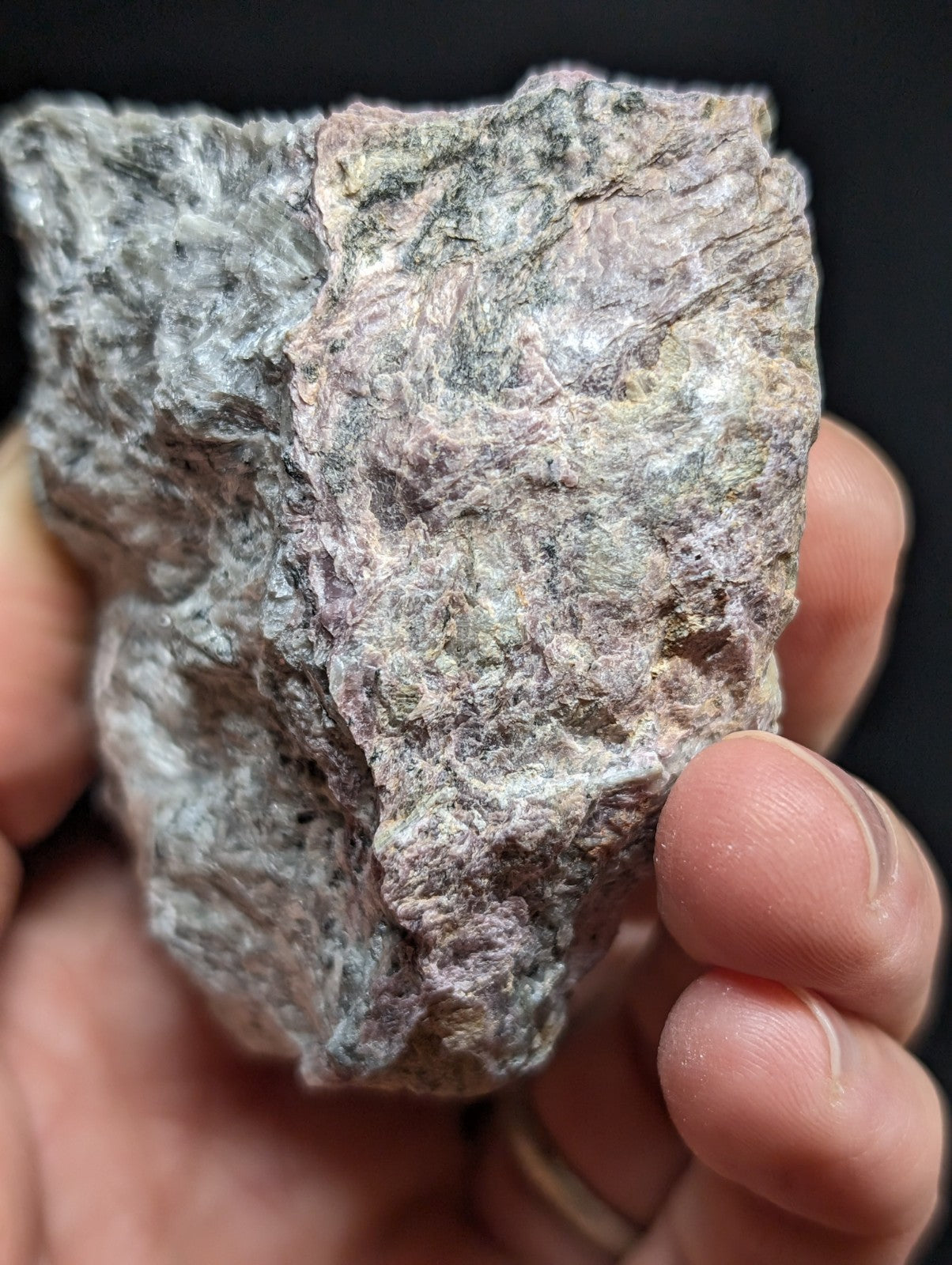 A rough, irregularly shaped rock with a mottled surface of gray, white, and subtle pinkish hues.