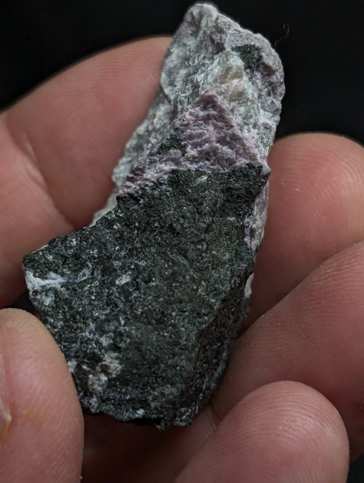 A rough, irregularly shaped mineral specimen with a dark green base and patches of white and purple veining.
