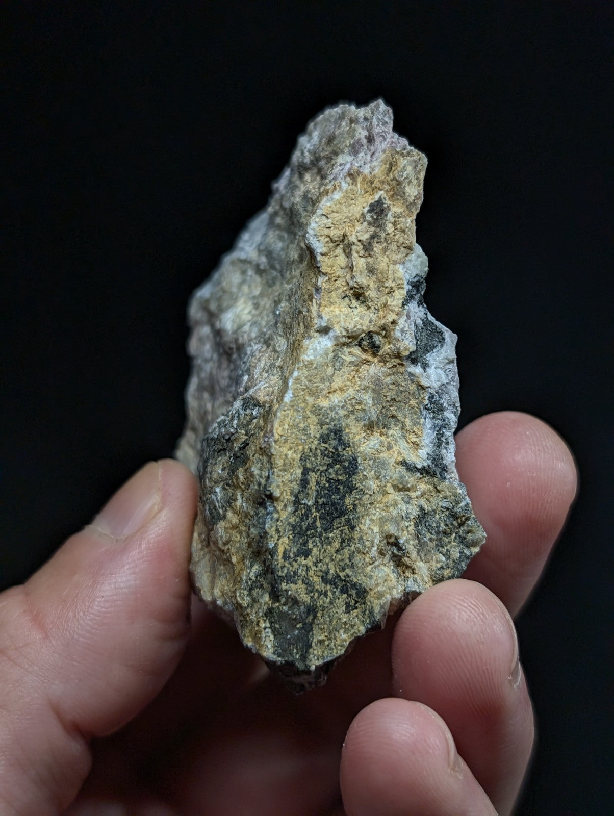 A rugged, irregularly shaped rock with a mottled surface of gray, black, and yellowish patches.