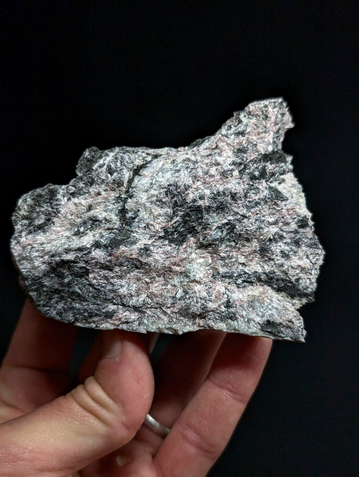 A hand holds a rough, irregularly shaped piece of gray and black speckled granite stone.