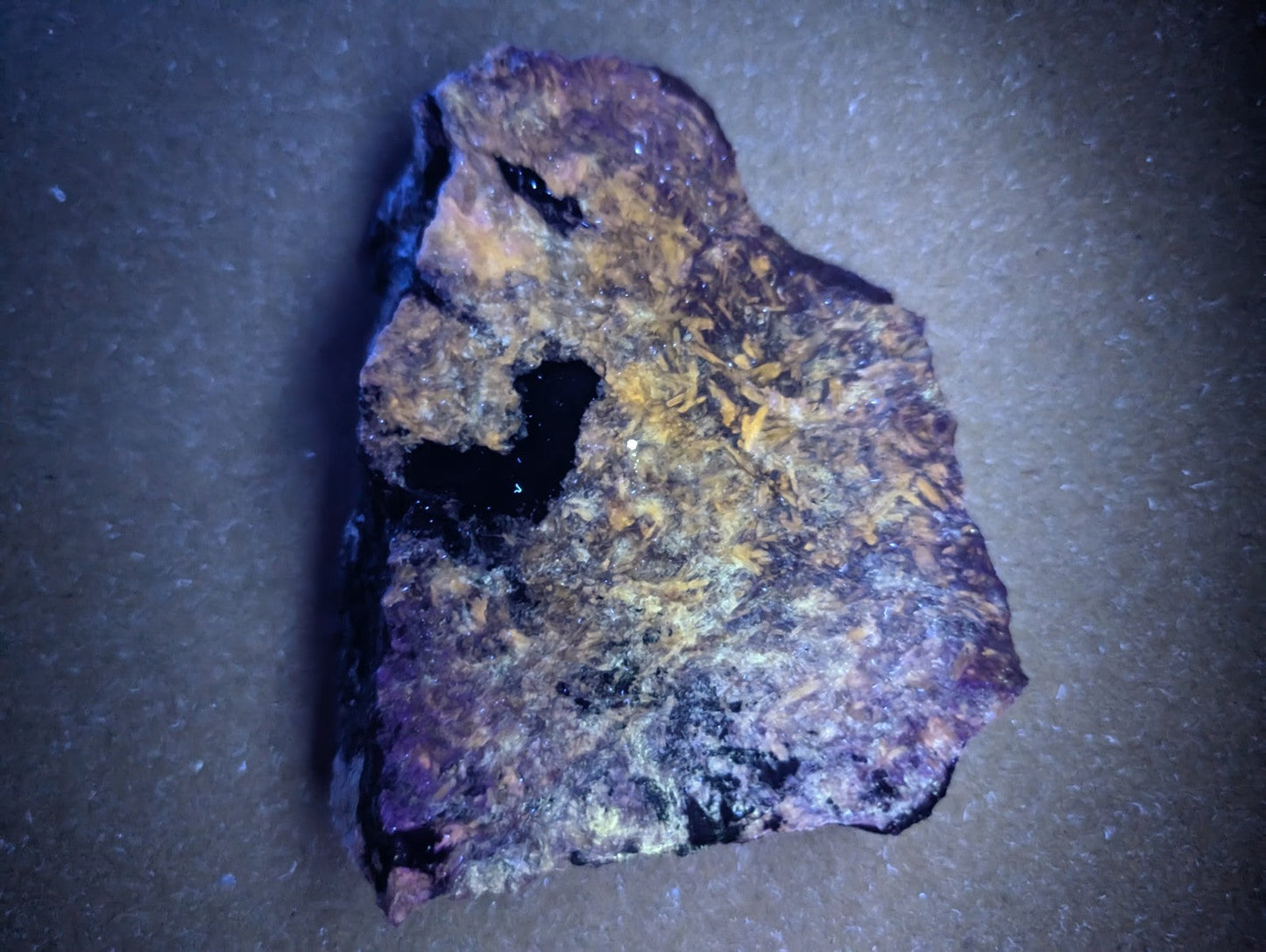 A rugged, irregularly shaped piece of mineral with a dark purple base and patches of yellowish-orange crystalline formations.