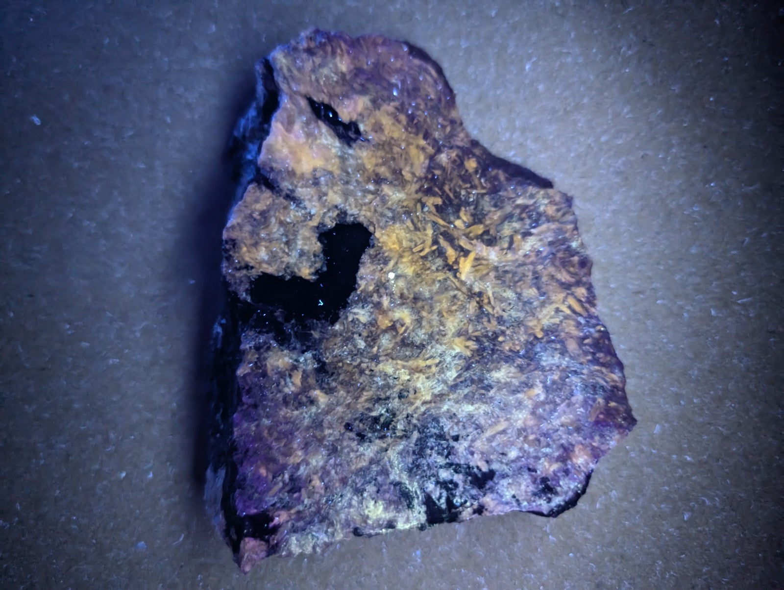 A rugged, irregularly shaped piece of mineral with a dark purple base and patches of yellowish-orange crystalline formations.