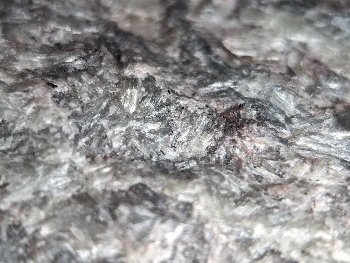 A textured, grayish-black stone surface with a crystalline pattern and subtle metallic sheen.