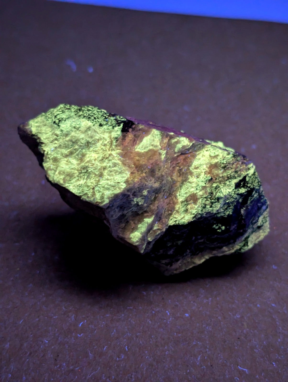 A rough miserite and wollastonite mineral specimen with vibrant fluorescent green coating and dark brown patches from arkansas
