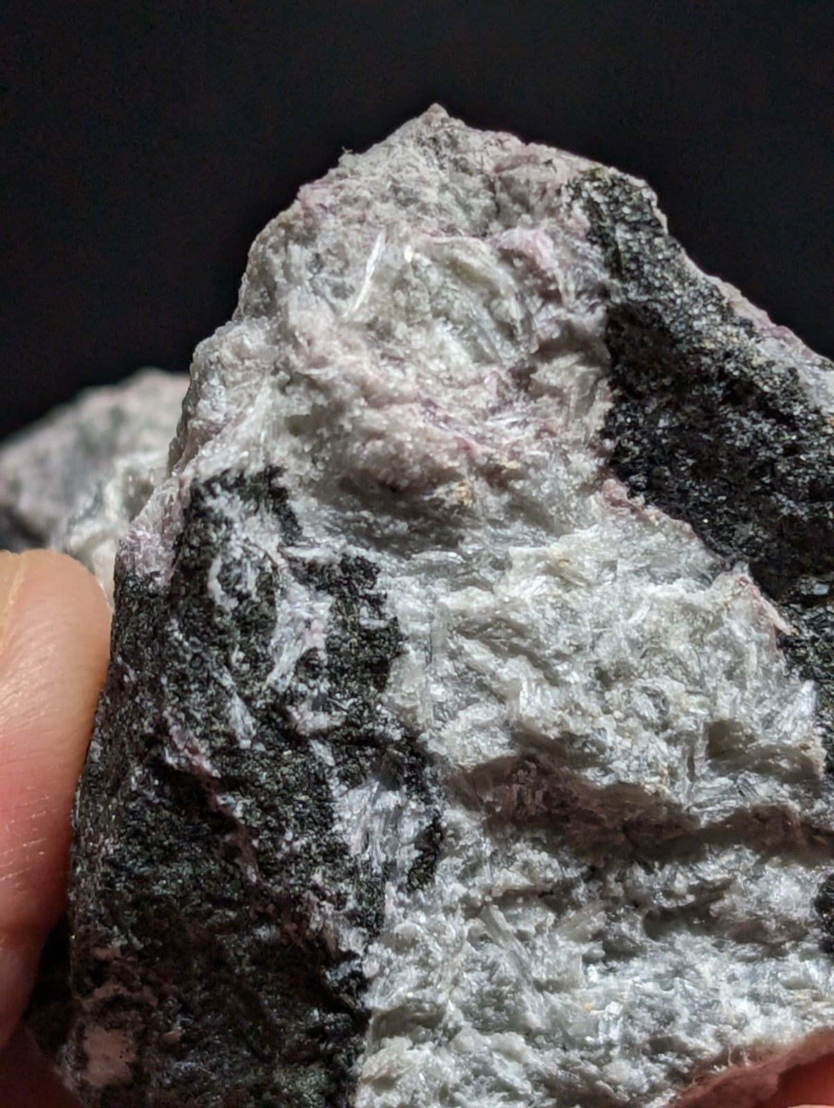 A rough, naturally occurring mineral specimen with a textured surface featuring patches of dark gray and light gray, accented by subtle pinkish hues.