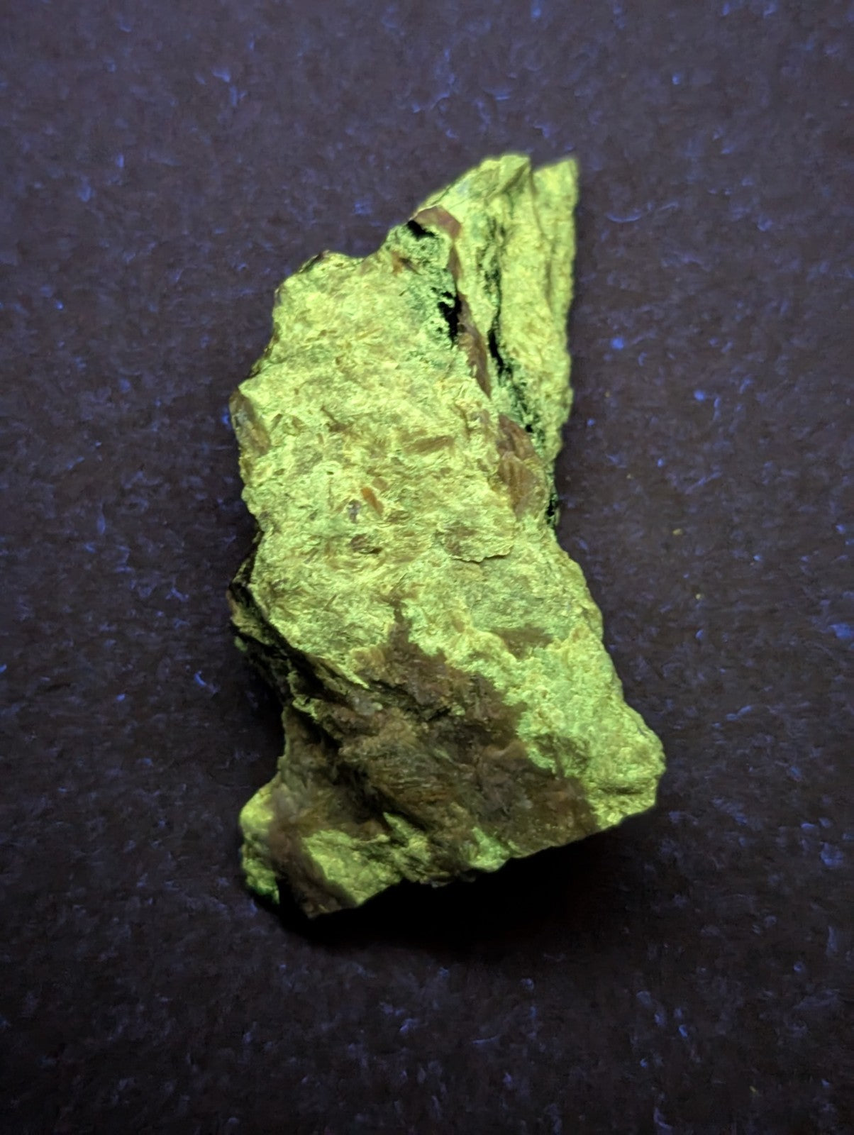 A rough, irregularly shaped piece of bright green mineral with patches of darker brown and black veining.