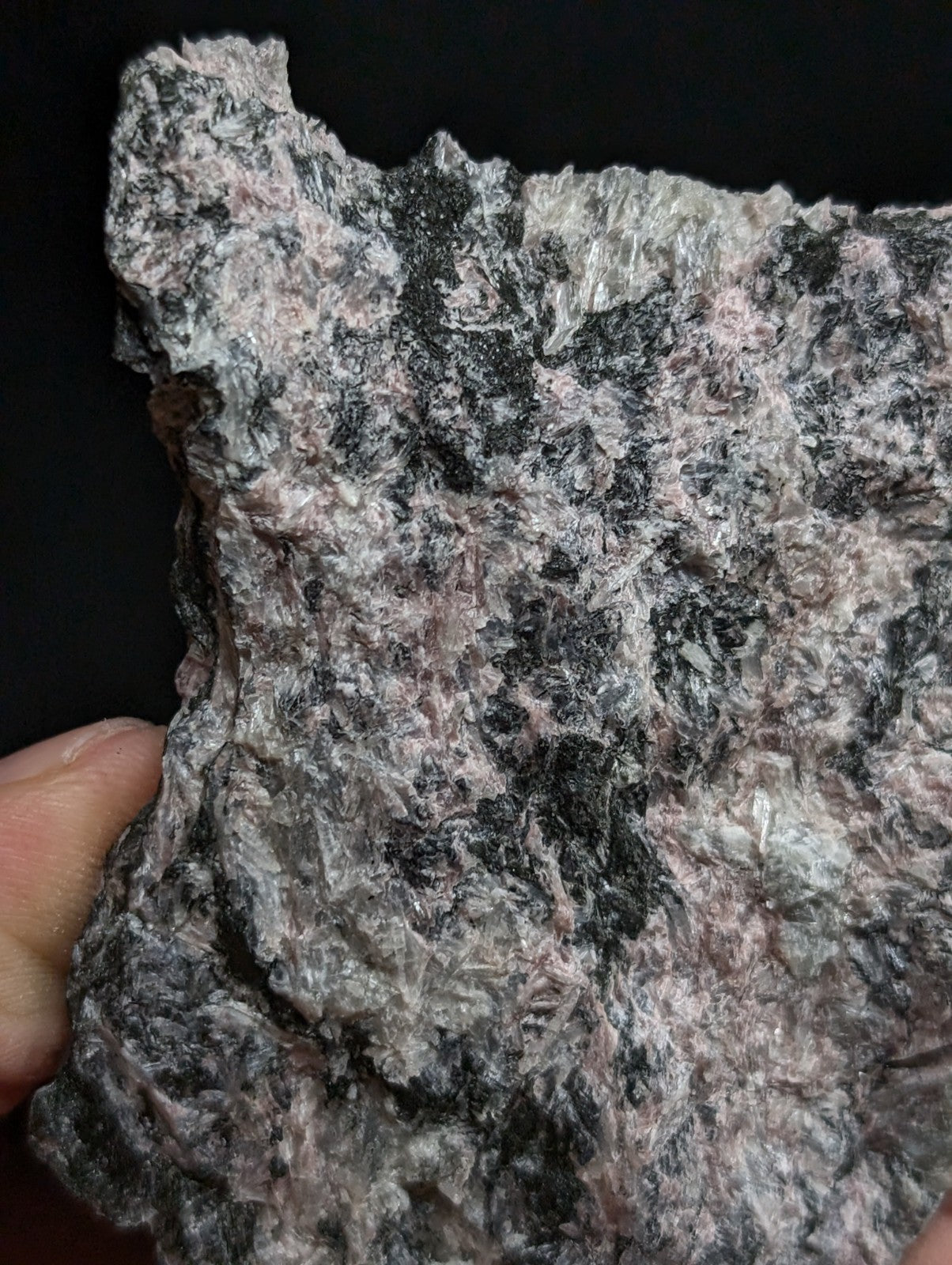 A rough, irregularly shaped piece of pink and black speckled rock held in a hand.