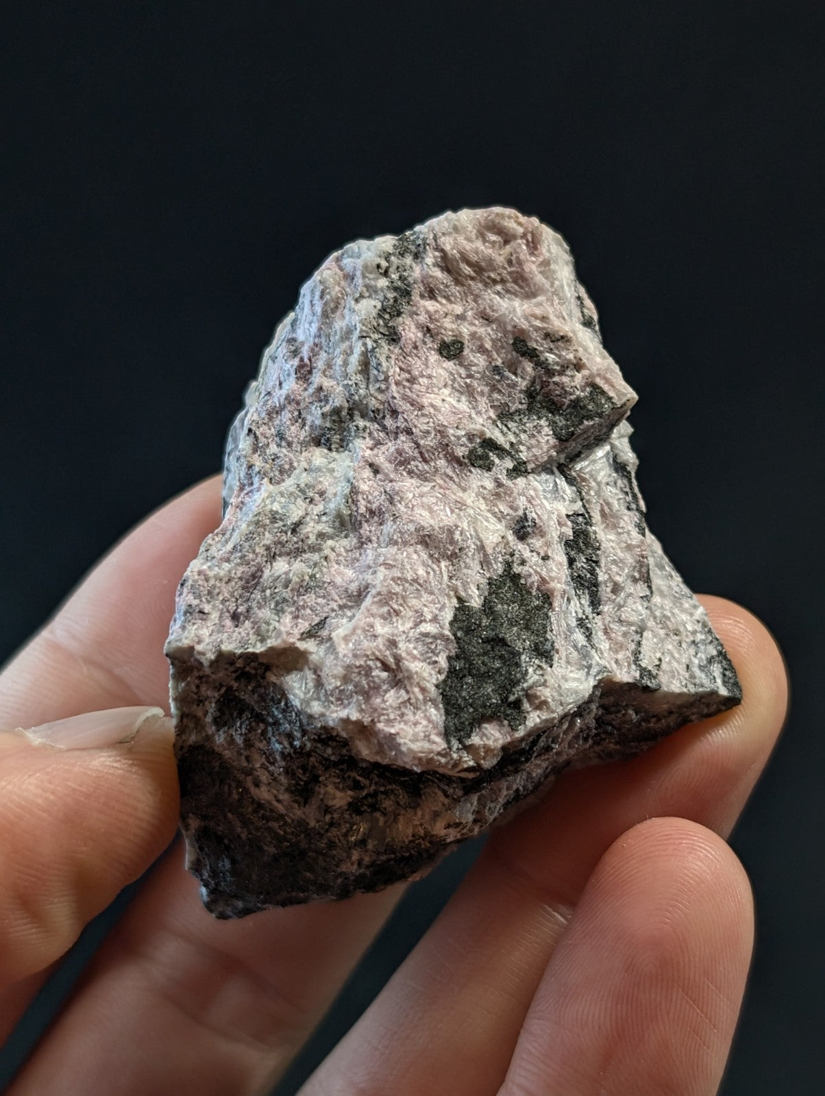 A rough, irregularly shaped rock with a mottled surface of light pinkish-gray and dark green patches.