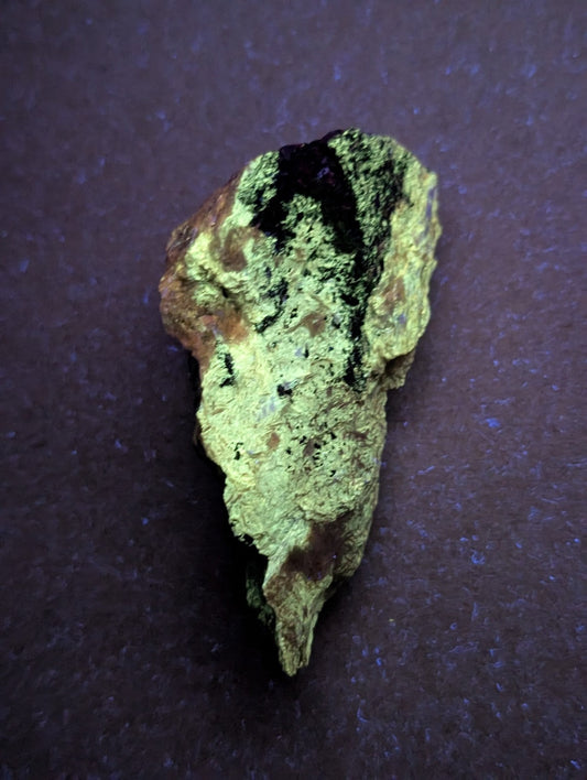 A rough, irregularly shaped mineral specimen with a mottled green and brown surface, featuring patches of dark black veining.