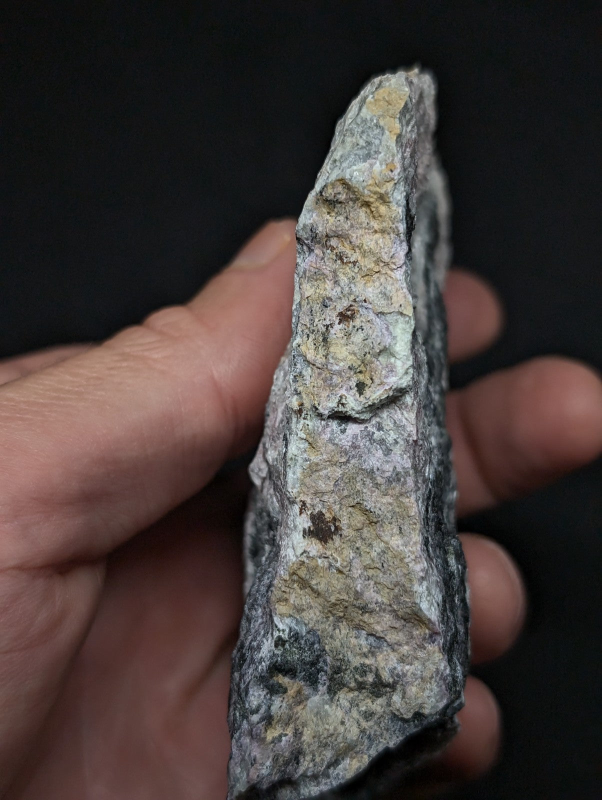 A rugged, irregularly shaped rock with a mottled surface of gray, white, and patches of yellowish-green mineral.