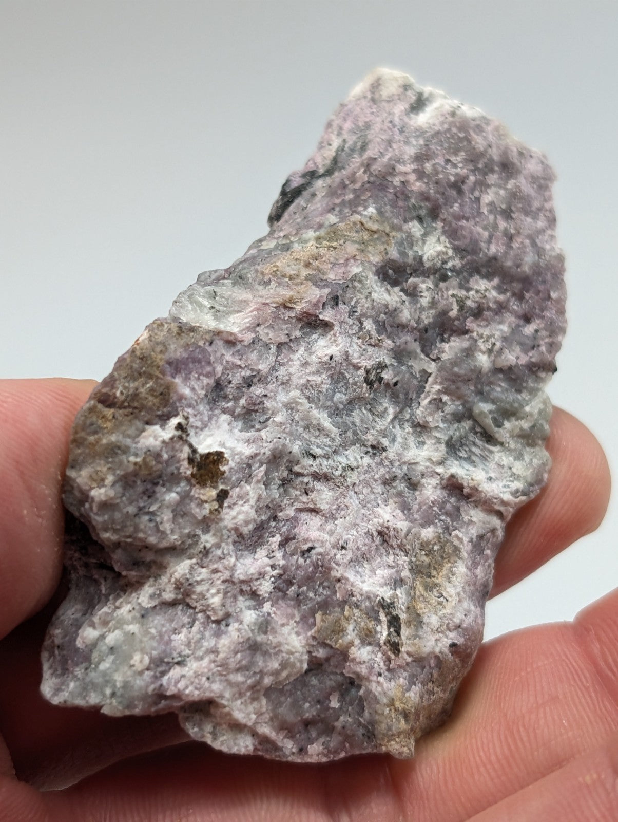 A rough, irregularly shaped purple and gray mineral specimen with a textured surface held in someone’s hand.