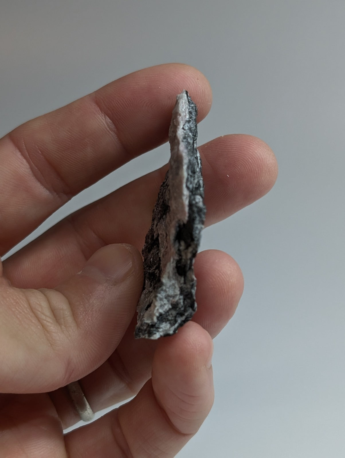 A jagged, irregularly shaped piece of dark gray and white mineral rock held in a hand.