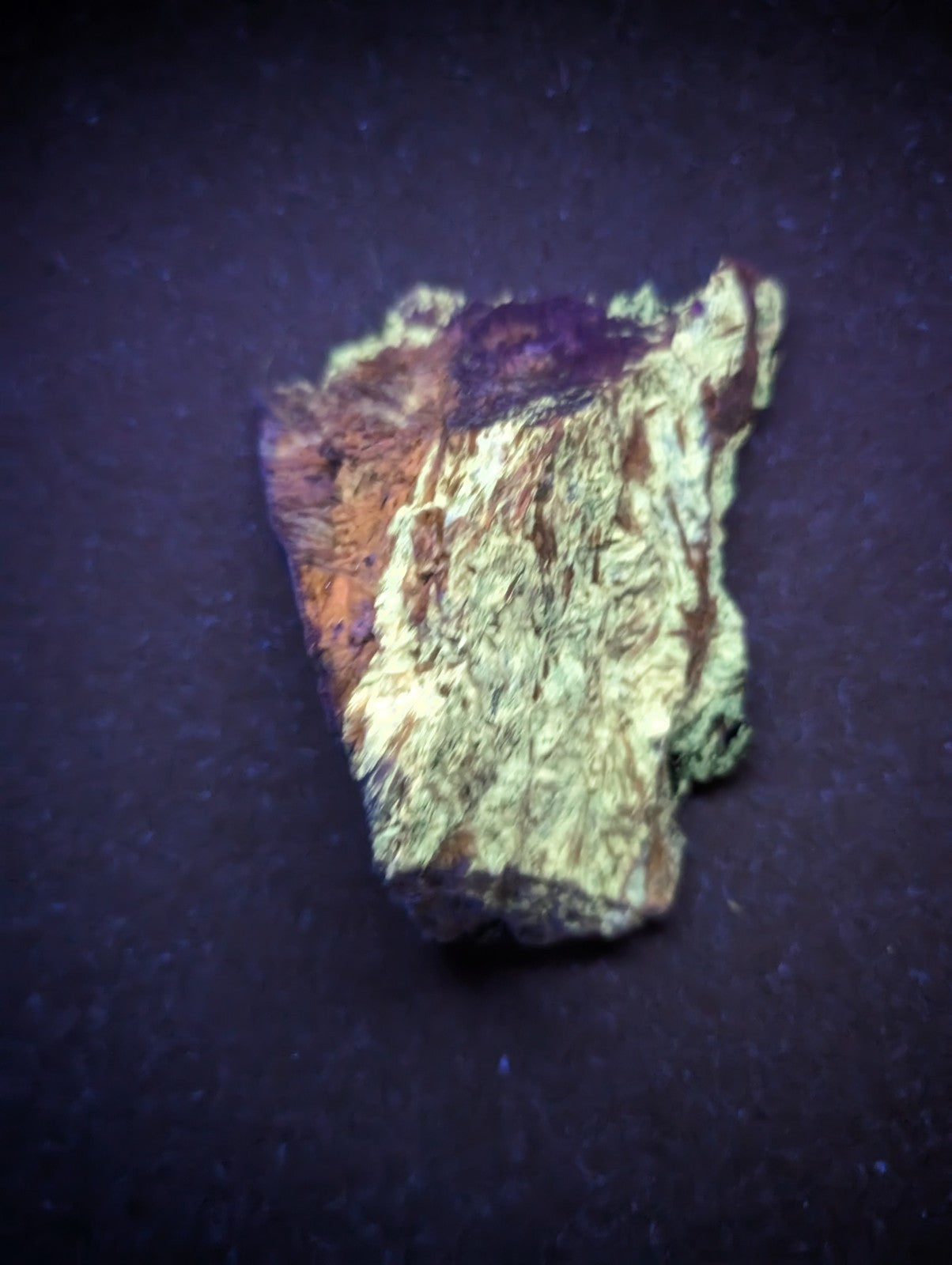 A rough, irregularly shaped mineral specimen with a textured surface displaying patches of vibrant purple, orange, and green hues.