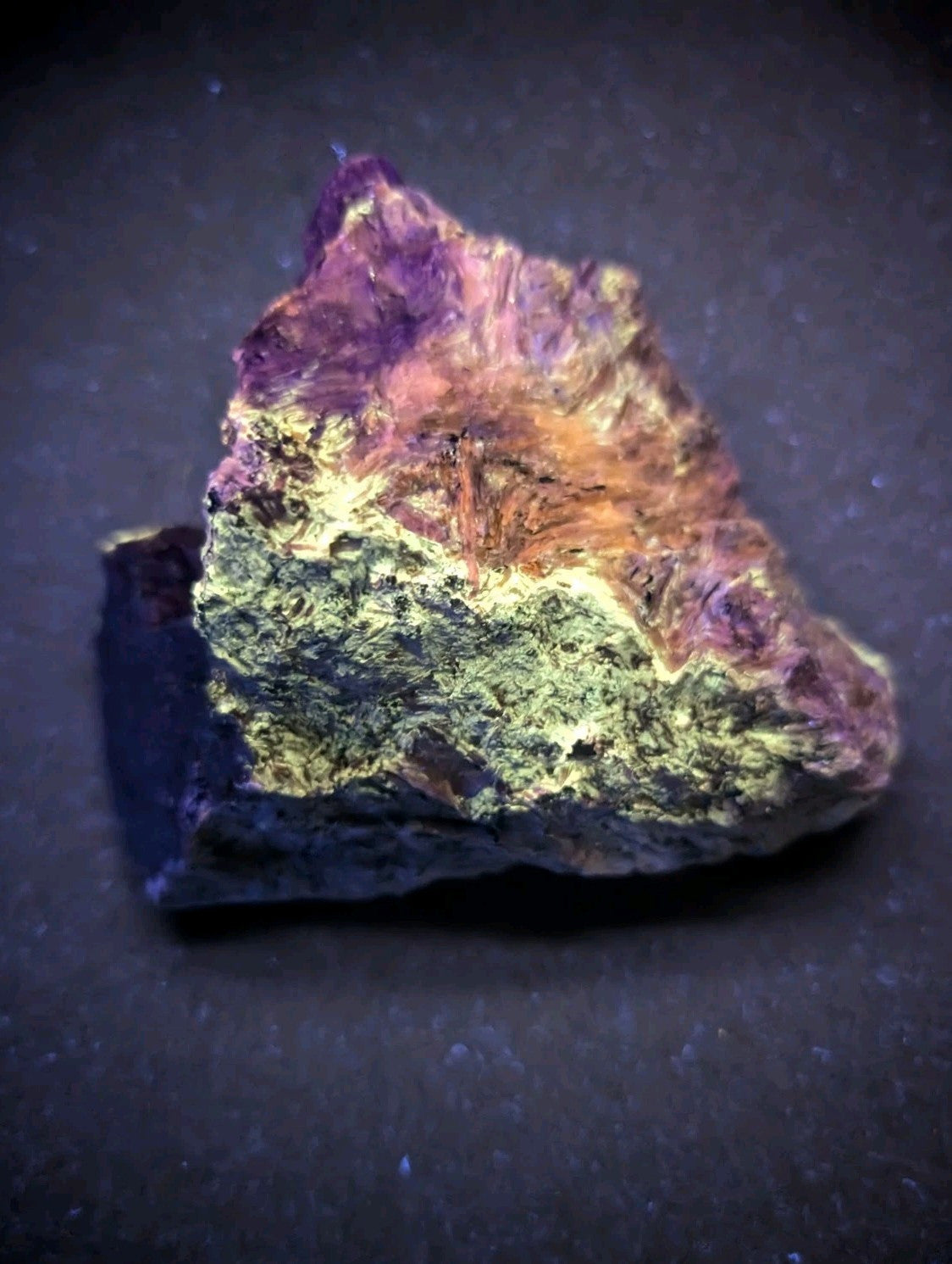 A vibrant, naturally occurring mineral specimen with a striking gradient of purple, orange, and green hues across its rough, textured surface.