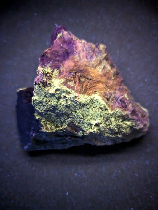 A vibrant, naturally occurring mineral specimen with a striking gradient of purple, orange, and green hues across its rough, textured surface.