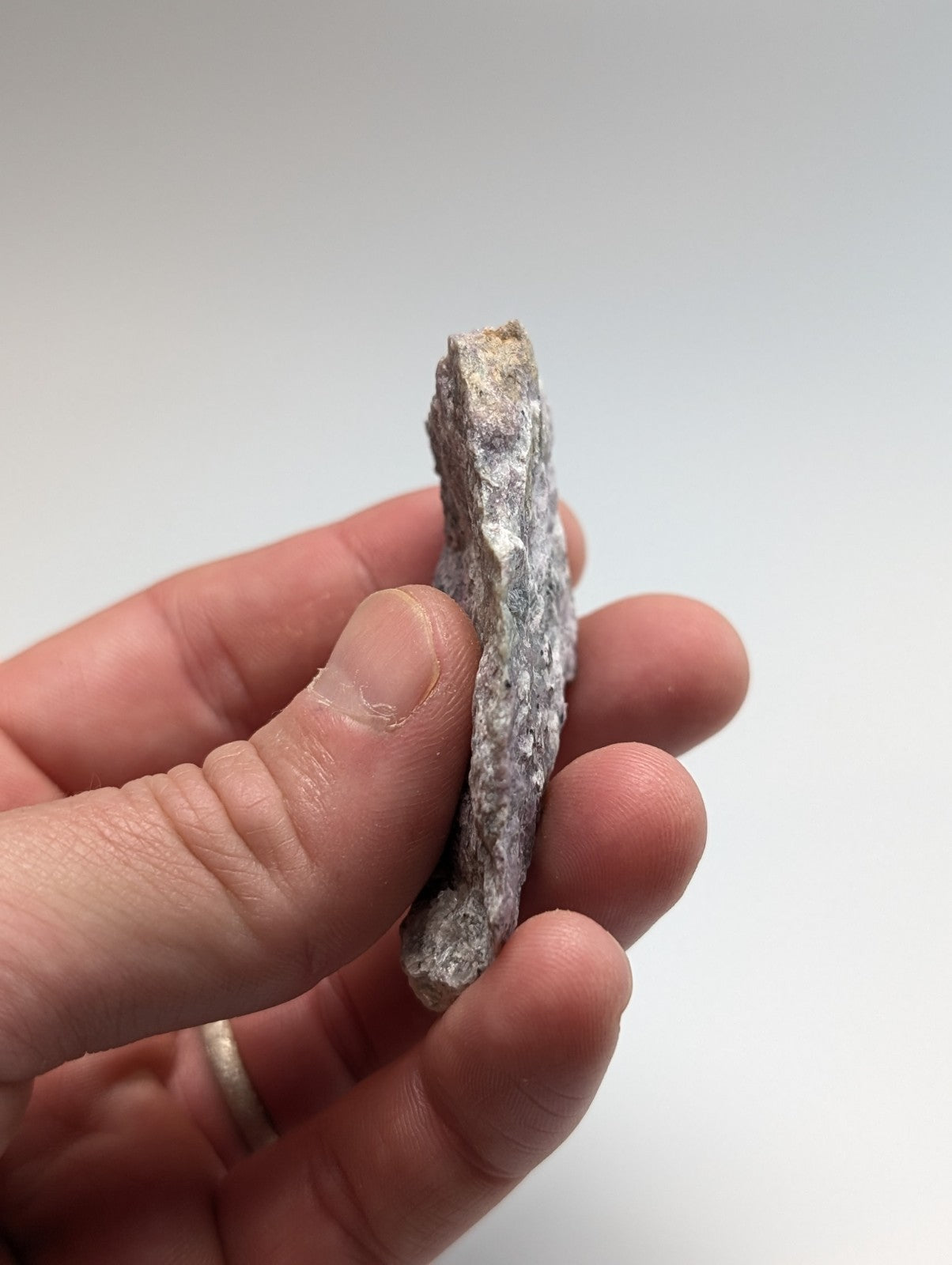 A rough, grayish-white mineral specimen with a textured, uneven surface held in someone’s hand.