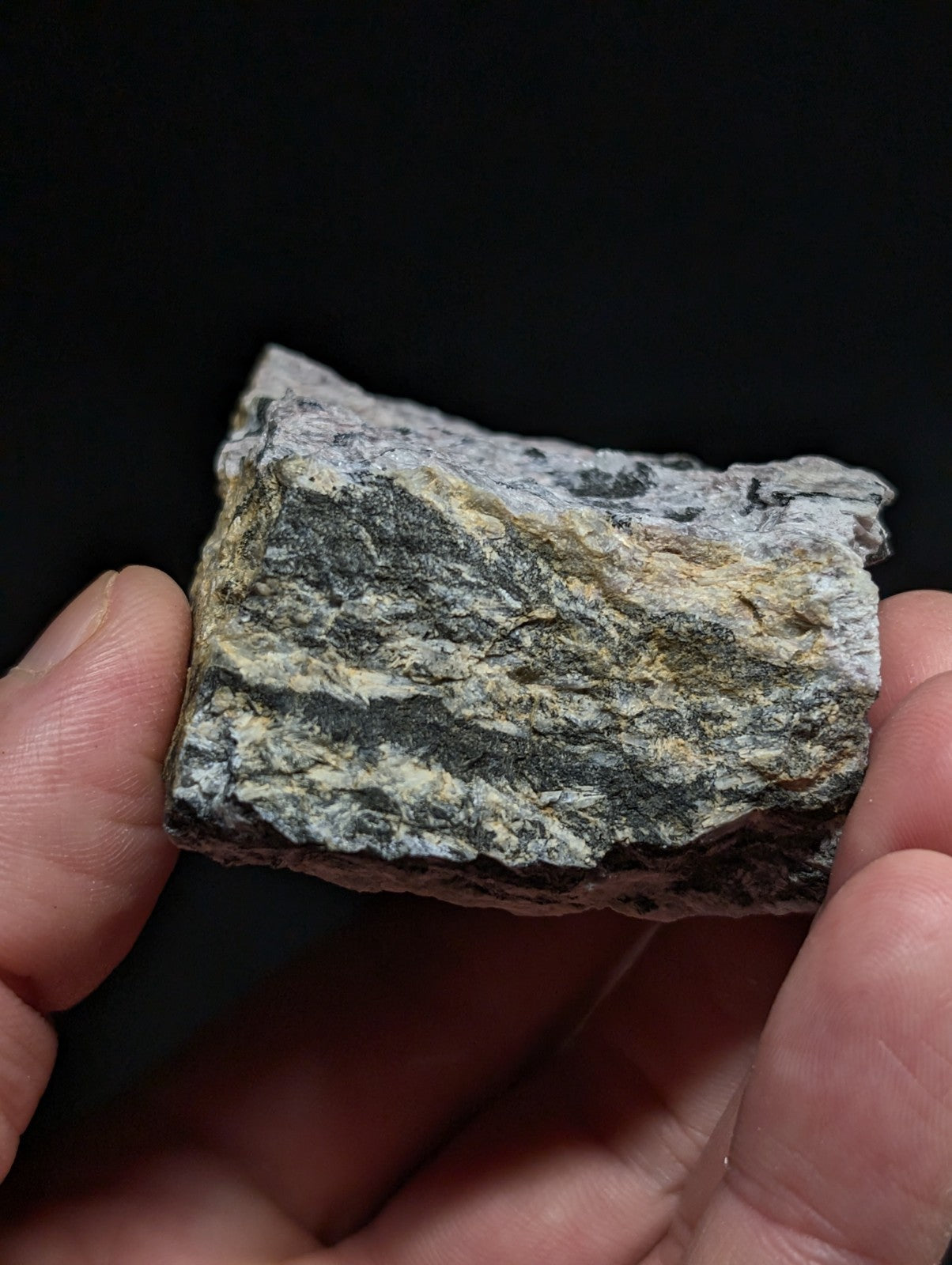 A rugged, irregularly shaped rock with a mottled pattern of gray, black, and faint yellowish streaks.
