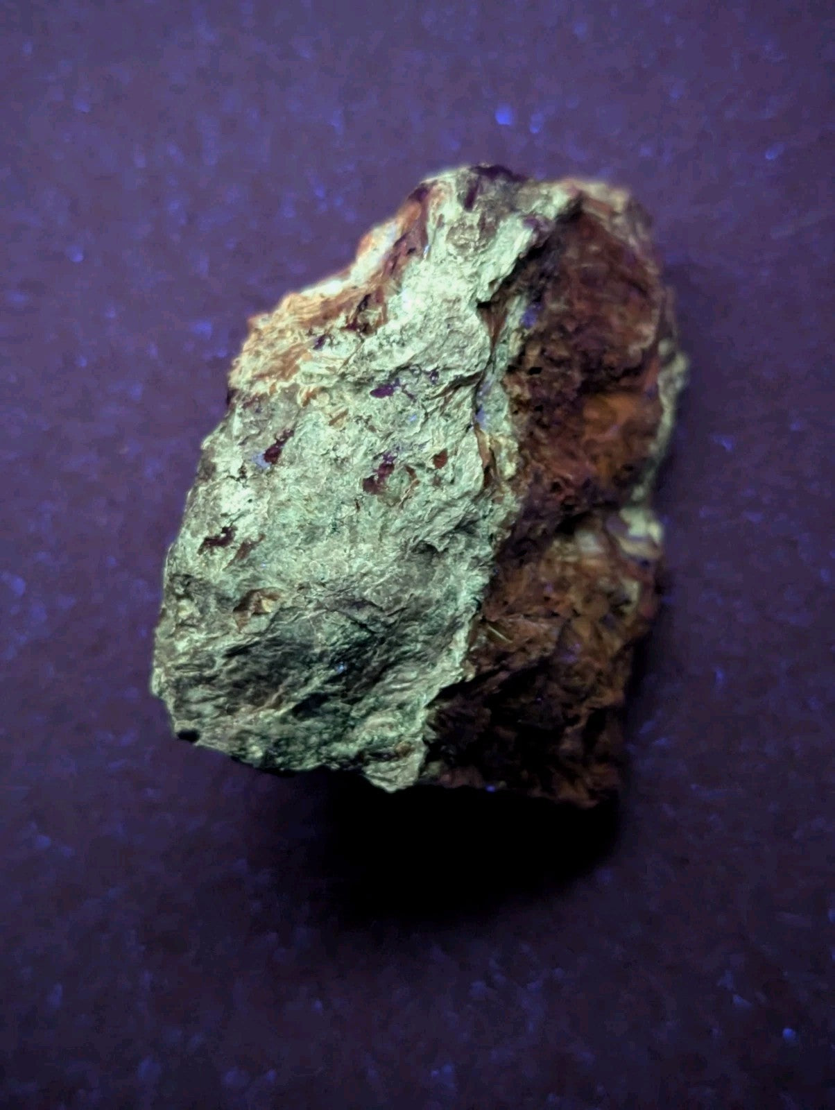 A rough, irregularly shaped mineral specimen with a greenish patina and patches of reddish-brown earthy material.