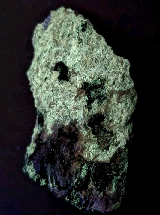 A rough, irregularly shaped mineral specimen with a textured surface displaying patches of greenish-white and dark black or purple hues.