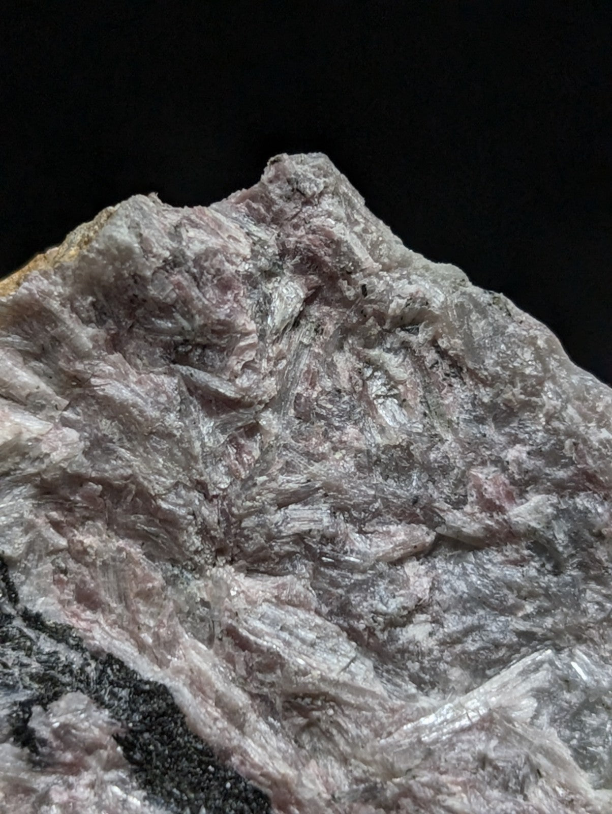 A rough, crystalline mineral specimen with a mix of gray and pale pink hues, featuring translucent, fibrous textures.