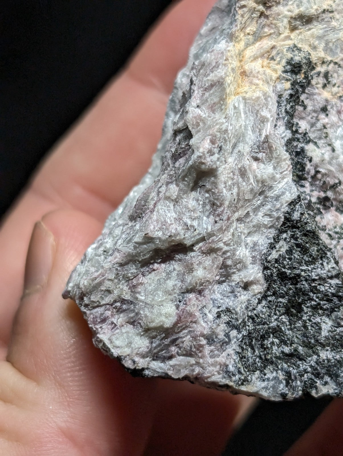 A rugged, naturally occurring rock specimen with a textured surface featuring patches of gray, black, and subtle hints of yellowish mineral streaks.