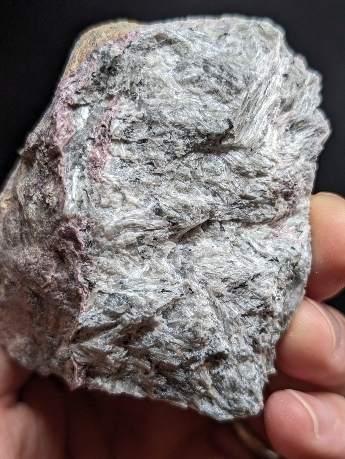 A rough, irregularly shaped mineral specimen with a textured surface displaying shades of gray and subtle pinkish hues.