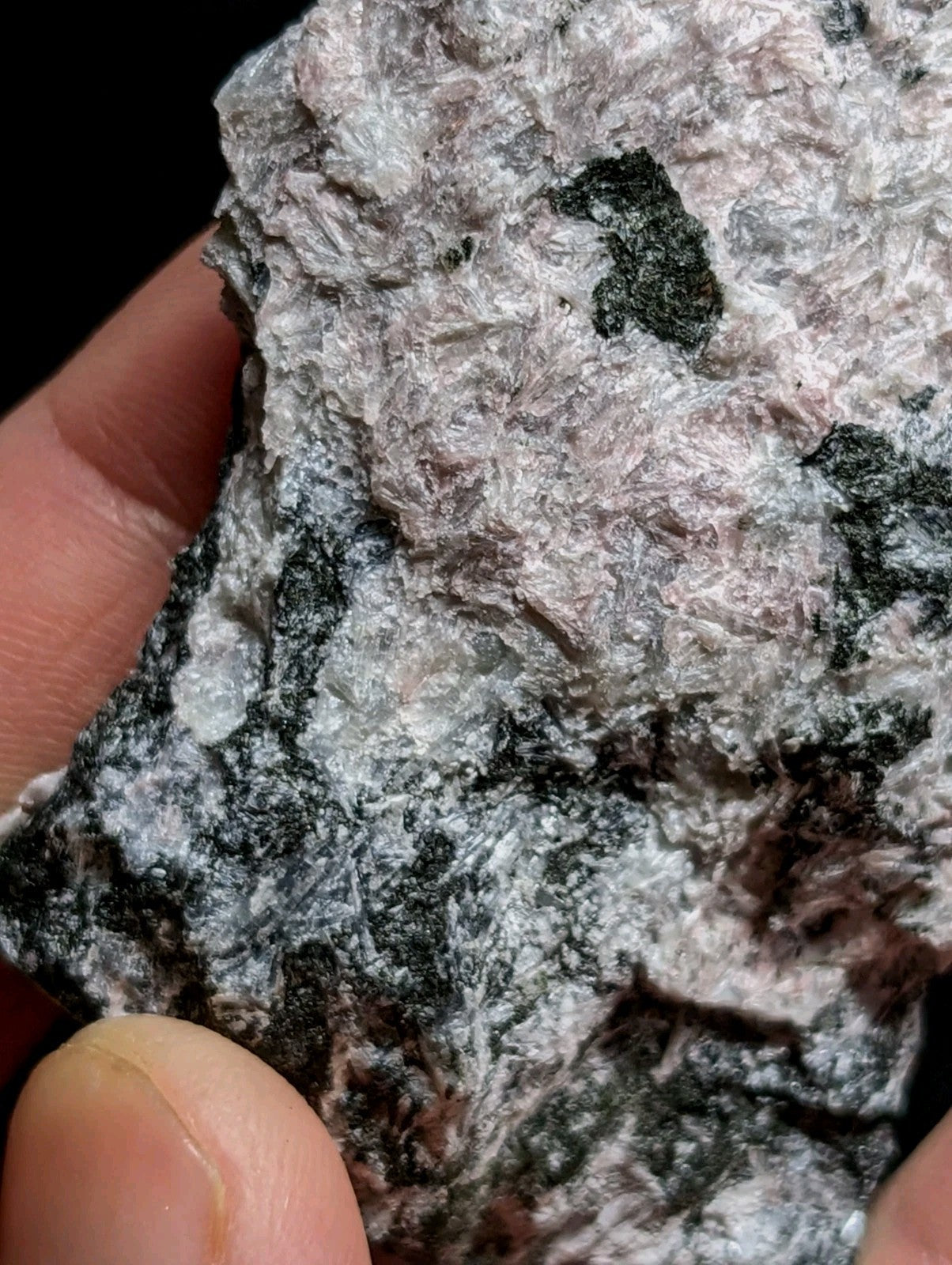 A rough, textured mineral specimen with a mottled pattern of gray, white, and dark green patches.