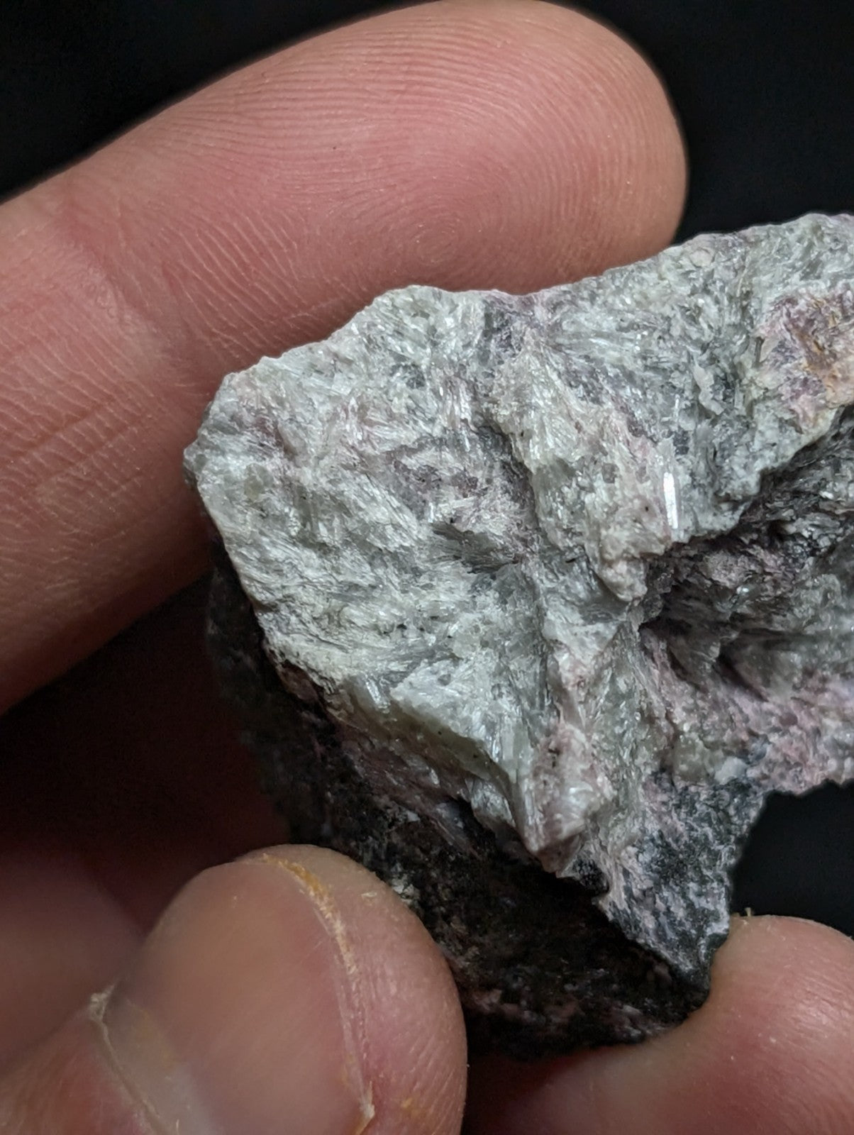A rough, irregularly shaped mineral specimen with a mottled gray and white surface, featuring subtle pinkish hues in its darker areas.