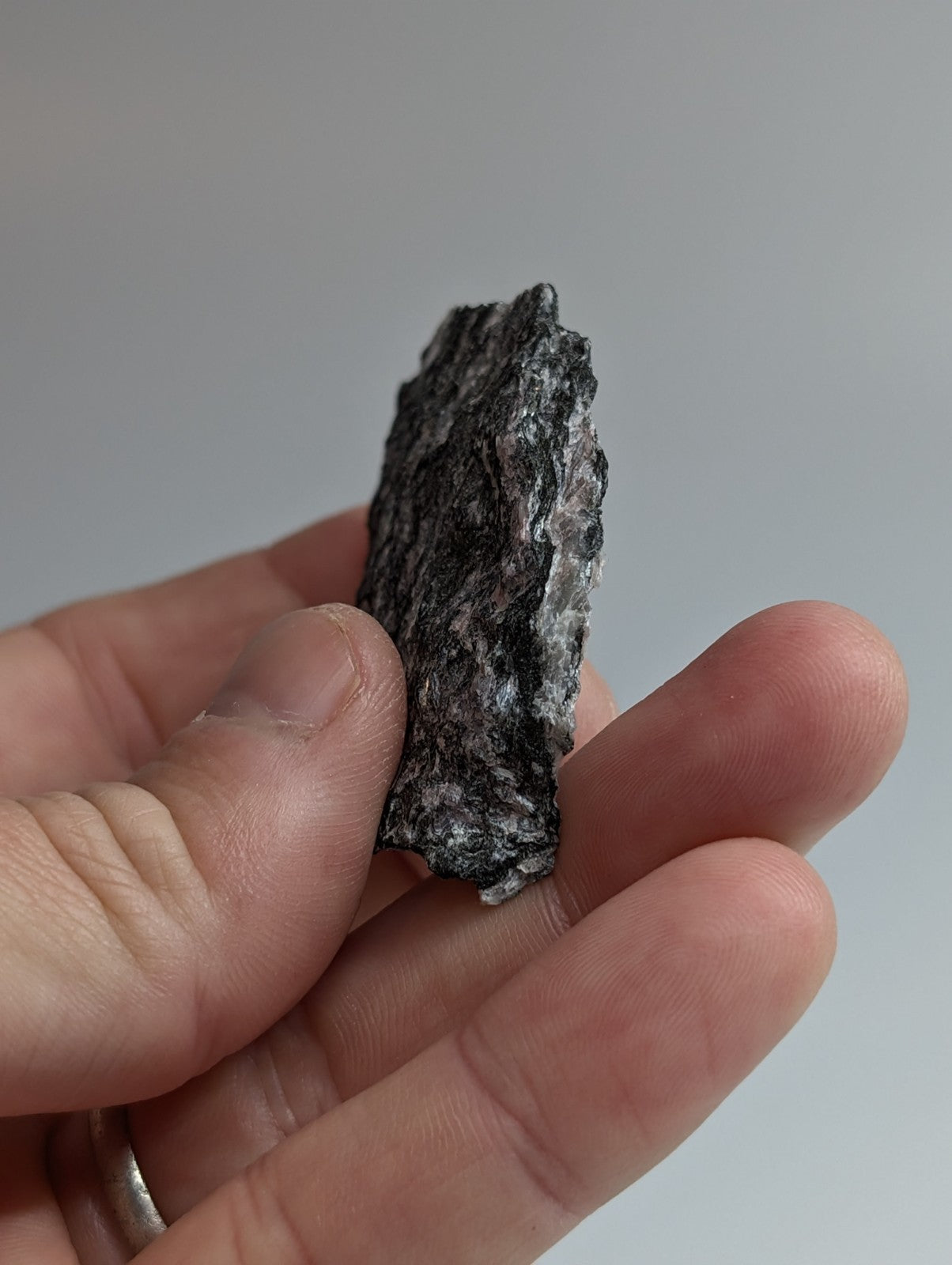 A dark, rough-textured rock with speckles of lighter gray and white held in a hand.