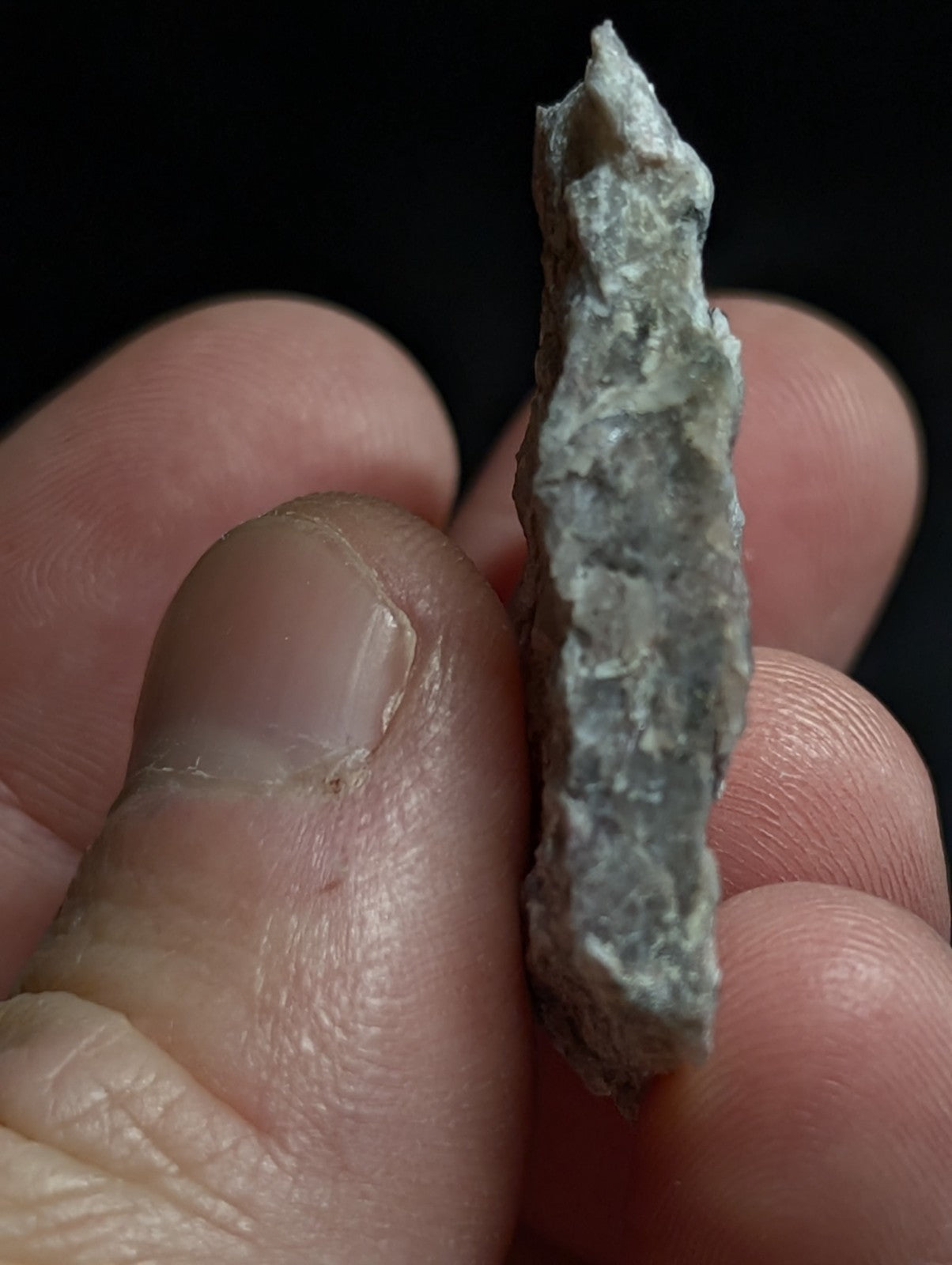 A rough, grayish-green stone fragment with a jagged edge and uneven surface.