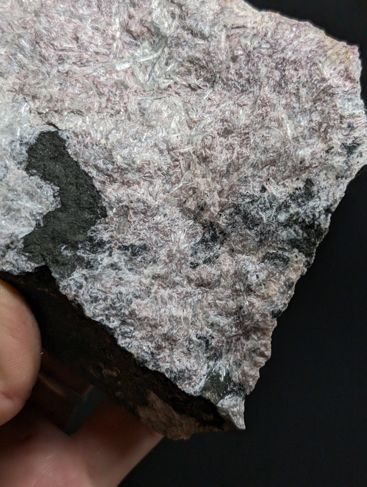A rough, irregularly shaped mineral specimen with a textured surface featuring fine white crystalline fibers embedded in a grayish matrix.