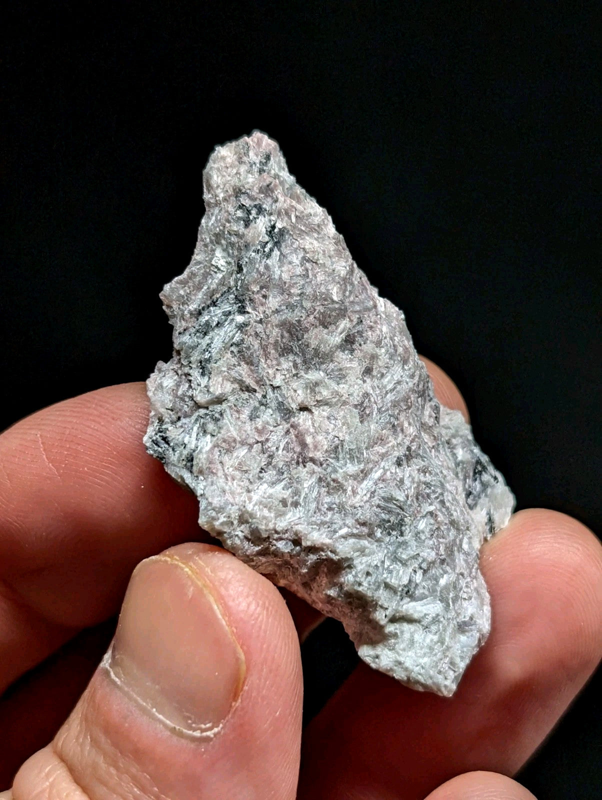 A rough, irregularly shaped gray rock with a textured surface held in someone’s hand.