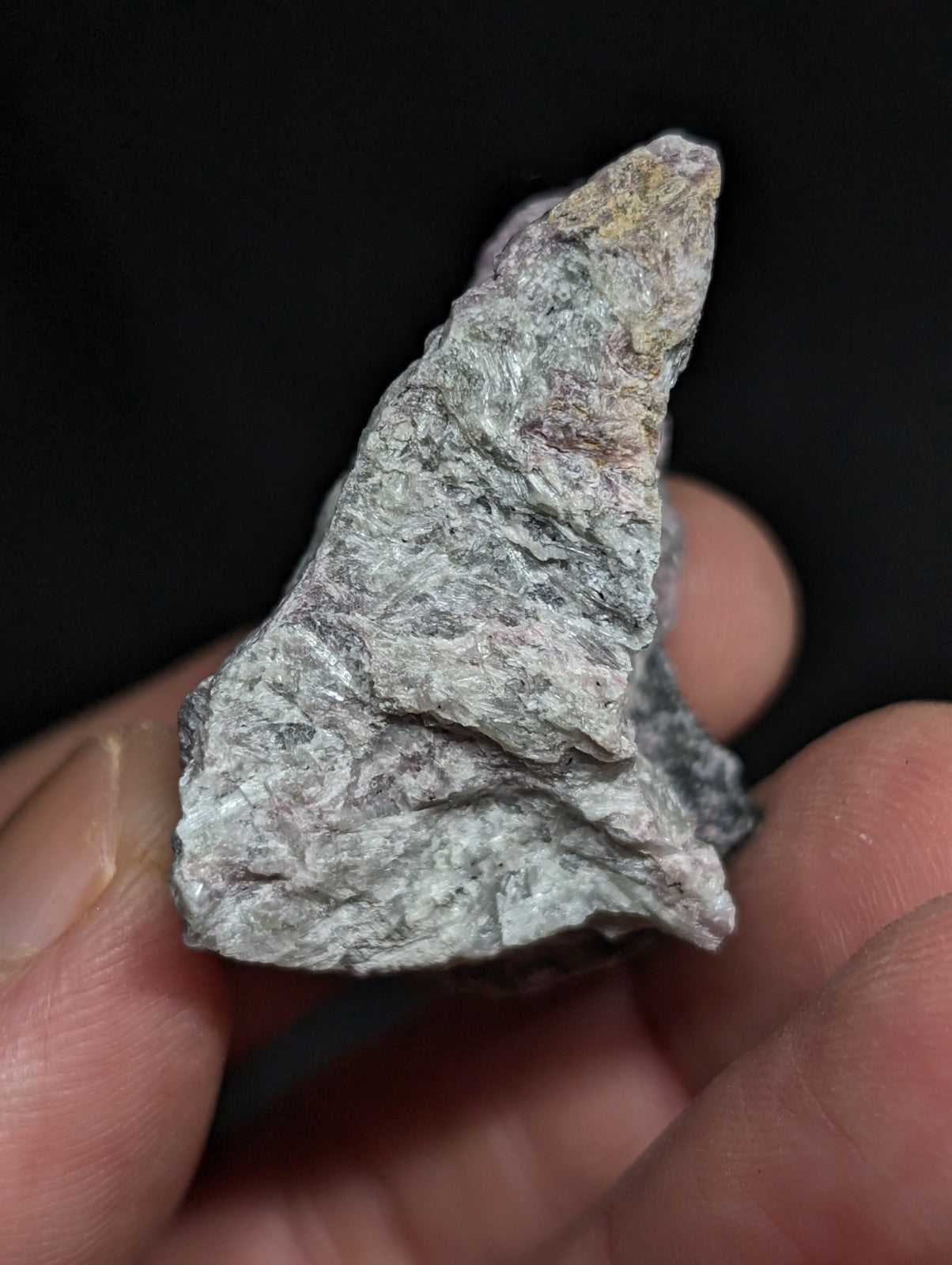A rough, irregularly shaped gray rock with subtle hints of green and brown speckles.